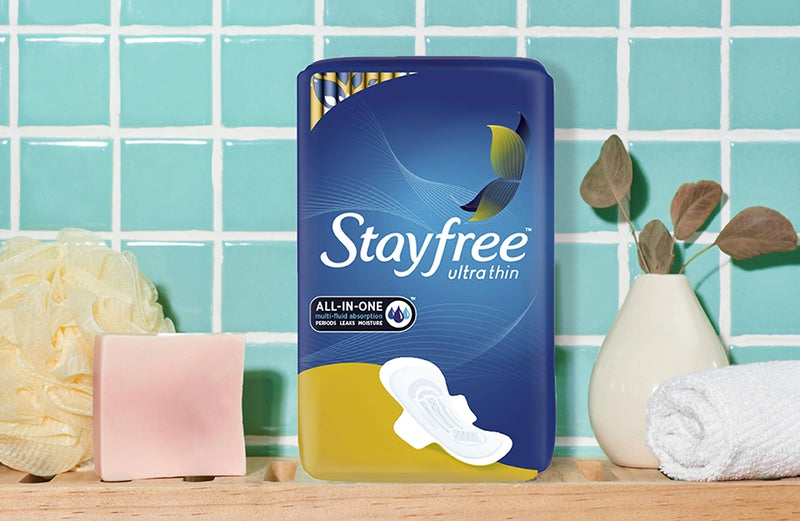 Stayfree Ultra Thin All-In-One pads in front of a tile bathroom wall, along with bar of soap, a towel and sponge